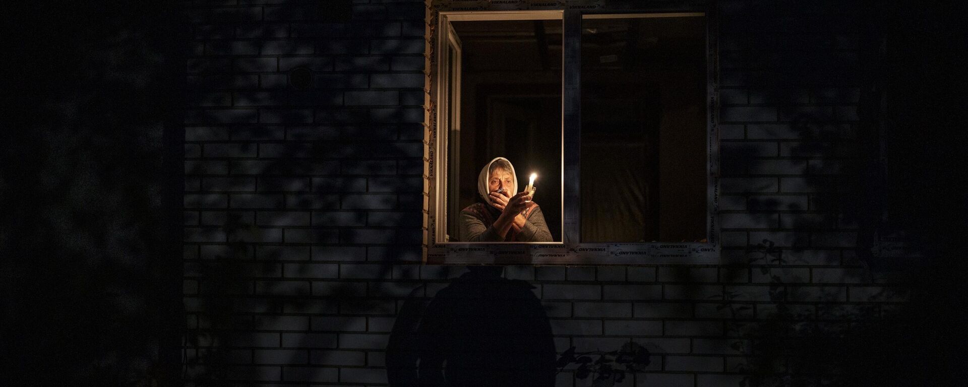 Mulher olha pela janela enquanto segura uma vela para iluminar sua casa durante uma queda de energia em Kiev. Ucrânia, 20 de outubro de 2022 - Sputnik Brasil, 1920, 16.11.2025