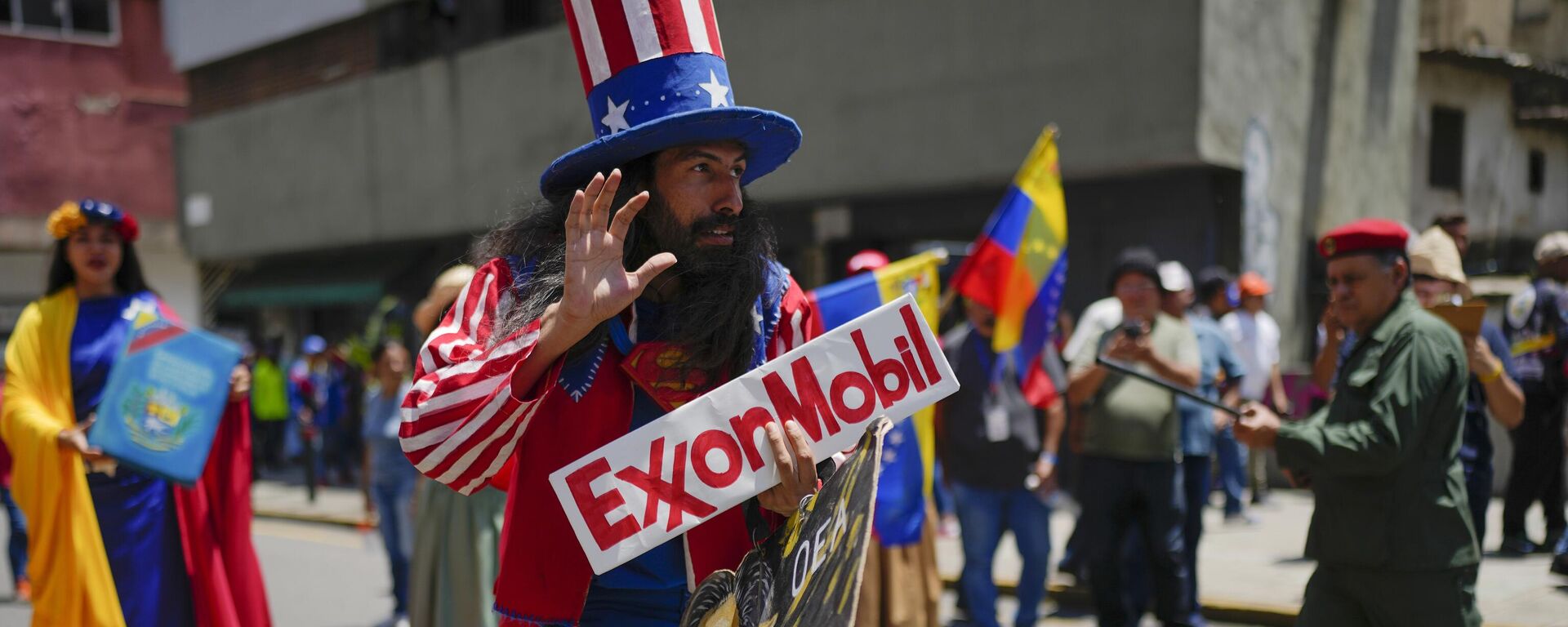 Homem vestido como o personagem norte-americano Tio Sam segura uma placa da petrolífera ExxonMobil durante a marcha pró-governo chamada Recupere Essequibo, em Caracas. Venezuela, 26 de setembro de 2023 - Sputnik Brasil, 1920, 26.09.2023