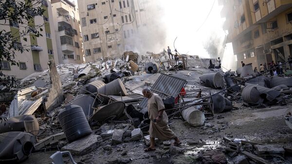 Palestinos caminham sobre escombros de prédio atingido por bombardeio israelense, 7 de outubro de 2023 - Sputnik Brasil