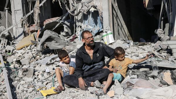 Homem palestino sentado com membros de sua família do lado de fora de um prédio destruído por um ataque aéreo israelense em Rafah. Faixa de Gaza, 12 de outubro de 2023 - Sputnik Brasil
