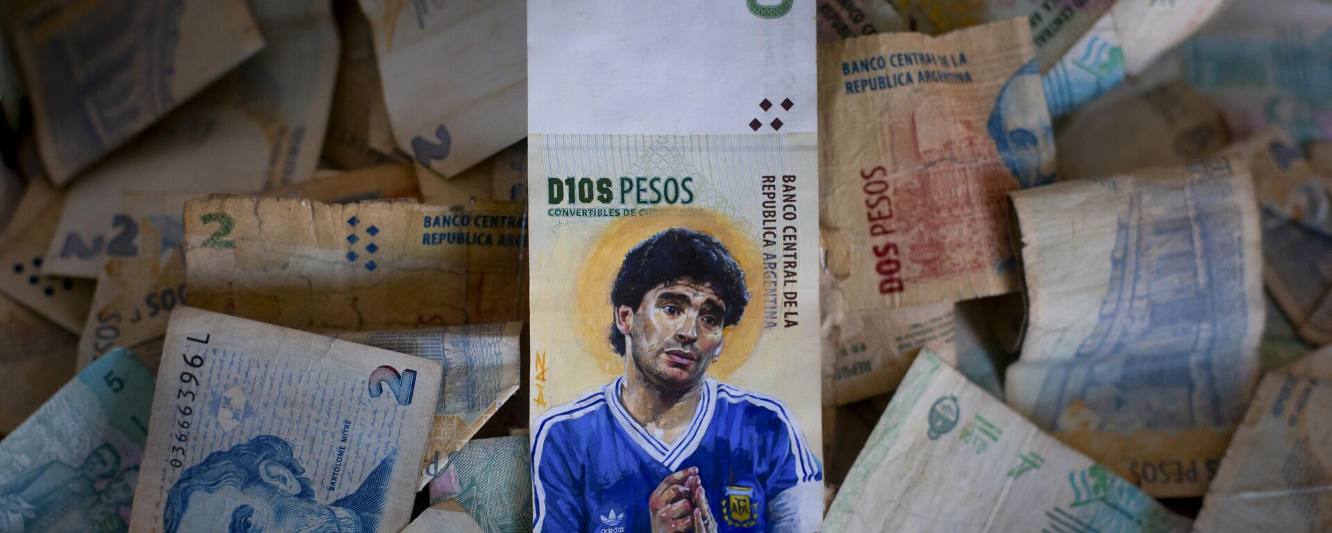 Uma peça arte do artista Sergio Díaz apresenta a falecida lenda do futebol Diego Maradona com as mãos envoltas em um rosário e uma auréola atrás da cabeça, pintada em uma nota de dez pesos argentinos em 9 de setembro de 2023 - Sputnik Brasil, 1920, 03.07.2024