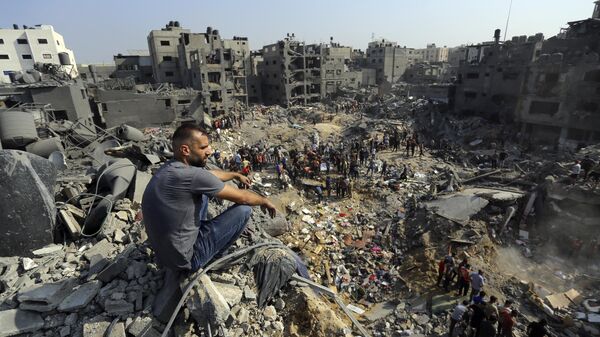 Homem senta-se sobre os escombros enquanto outros passeiam entre os destroços de edifícios alvos de ataques aéreos israelenses no campo de refugiados de Jabaliya, no norte da Faixa de Gaza, 1º de novembro de 2023 - Sputnik Brasil