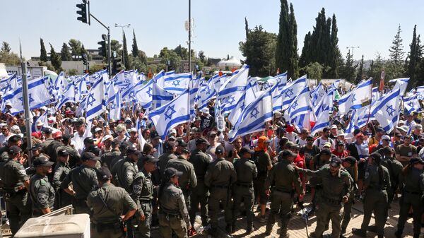 Forças de segurança israelenses montam guarda enquanto manifestantes agitam a bandeira nacional na entrada do Knesset em meio a uma onda de protestos que durou meses contra a planejada reforma judicial do governo,  em 24 de julho de 2023 - Sputnik Brasil