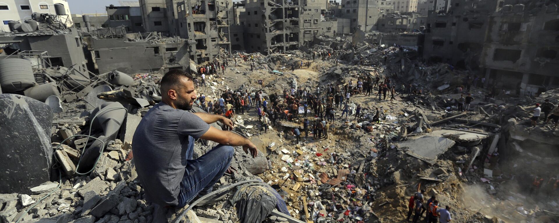 Homem sentado nos escombros enquanto outros vagam entre os destroços de edifícios que foram alvo de ataques aéreos israelenses no campo de refugiados de Jabalia. Faixa de Gaza, 1º de novembro de 2023 - Sputnik Brasil, 1920, 10.11.2023