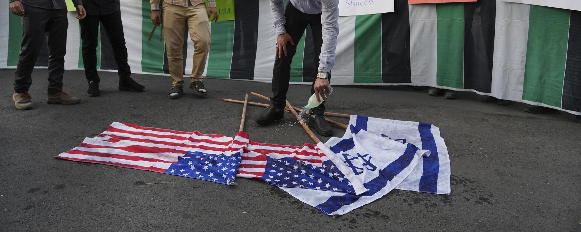 Manifestante derrama gasolina nas bandeiras de Israel e dos EUA, antes de atear fogo a elas, durante um protesto em Teerã contra a viagem de Biden ao Oriente Médio. Irã, 16 de julho de 2022 - Sputnik Brasil, 1920, 28.02.2024