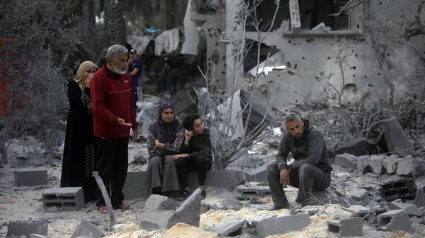 Palestinos se sentam sobre os escombros de uma casa destruída após ataques aéreos israelenses na cidade de Khan Yunis. Faixa de Gaza, 22 de novembro de 2023 - Sputnik Brasil