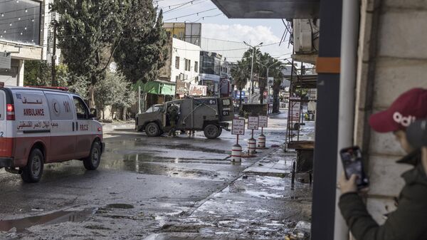 Jovens palestinos observam carro de patrulha do Exército israelense da segurança, durante combates entre Israel e o grupo palestino Hamas, na entrada do campo de refugiados de Jenin, na Cisjordânia ocupada, em 13 de dezembro de 2023 - Sputnik Brasil