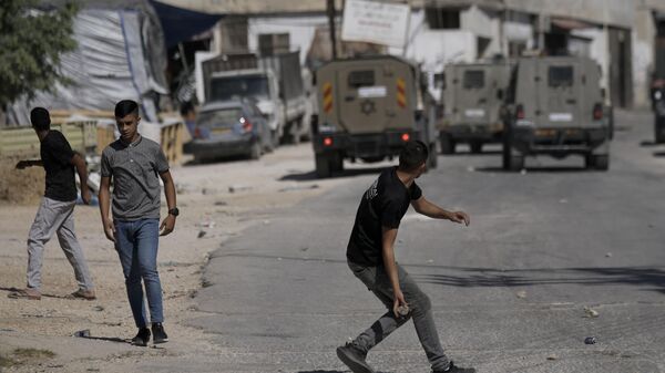 Palestinos atiram pedras em veículo militar israelense que participa de incursão militar no campo de refugiados de Askar, na cidade de Nablus, na Cisjordânia, em 24 de julho de 2023 - Sputnik Brasil