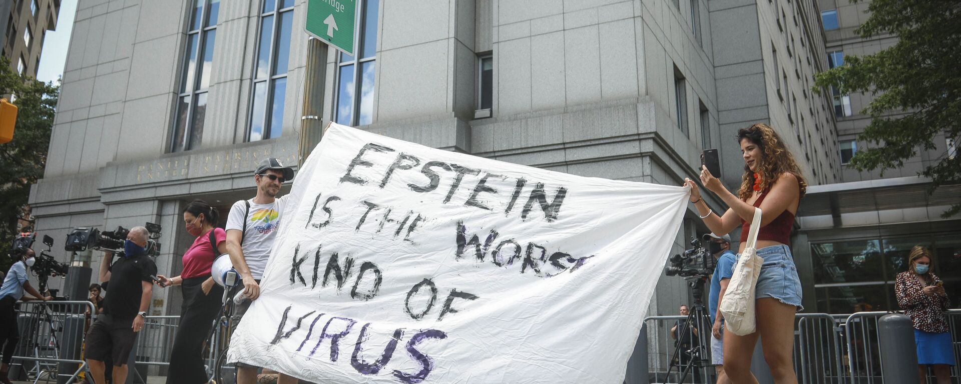 A artista multimídia Katelyn Kopenhaver (D), com a ajuda de seu irmão Brent Kopenhaver, desenrola um banner que diz [Jefferey] Epstein é o pior tipo de vírus, do lado de fora do tribunal federal, onde um juiz realizou uma audiência de fiança por vídeo para a ex-namorada de Epstein, Ghislaine Maxwell, em Nova York, 14 de julho de 2020 - Sputnik Brasil, 1920, 18.07.2025