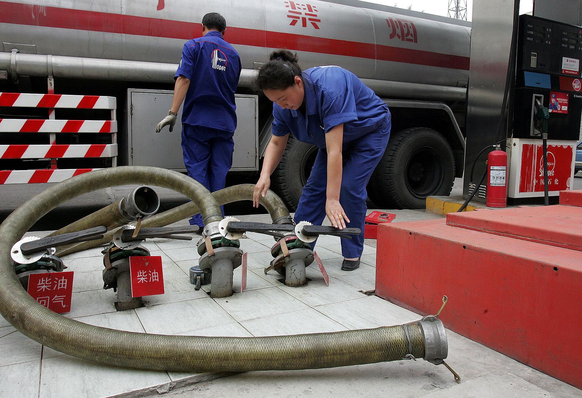 Trabalhador chinês de uma das maiores empresas de petróleo da China, a Sinopec, manuseia mangueiras após entregar gasolina em um posto em Pequim, China - Sputnik Brasil, 1920, 30.08.2024