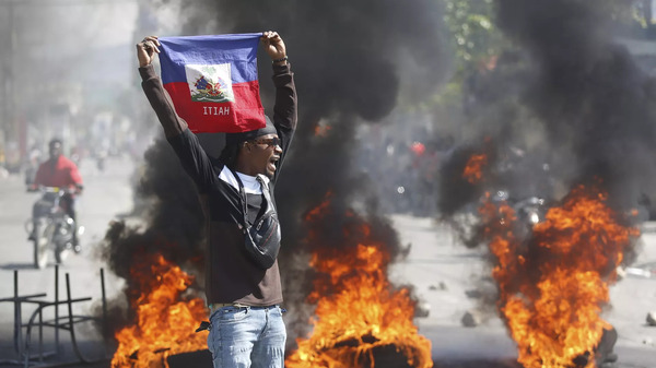 Manifestante segura bandeira do Haiti durante protesto que pede a saída do primeiro-ministro, Ariel Henry, em meio à escalada da violência no país. Porto Príncipe, 2 de março de 2024 - Sputnik Brasil
