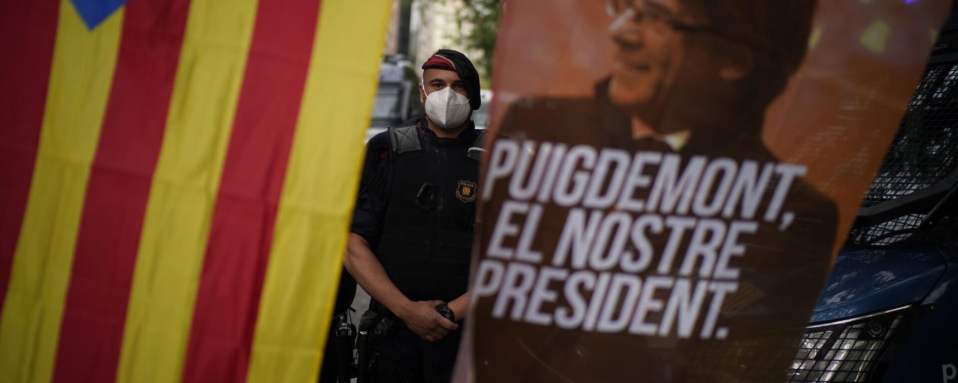 Policial atrás de uma bandeira da Catalunha e uma faixa com a imagem do ex-líder catalão Carles Puigdemont com a mensagem Puigdemont, nosso líder. Espanha, 24 de setembro de 2021 - Sputnik Brasil, 1920, 16.05.2024