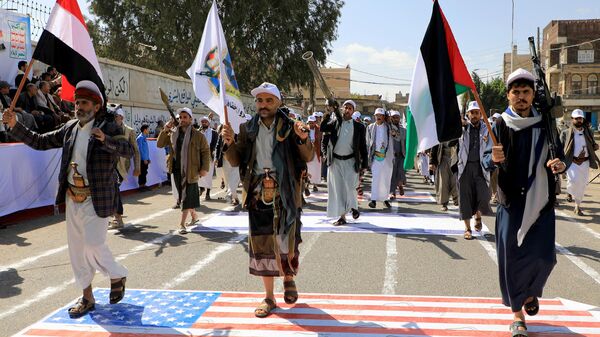 Iemenitas armados passam por cima de uma bandeira dos EUA e de Israel pintada no asfalto na capital controlada pelos houthi, Sanaa, durante uma marcha em apoio aos palestinos em meio a batalha em curso entre militantes de Israel e do Hamas na Faixa de Gaza, 29 de fevereiro de 2024 - Sputnik Brasil