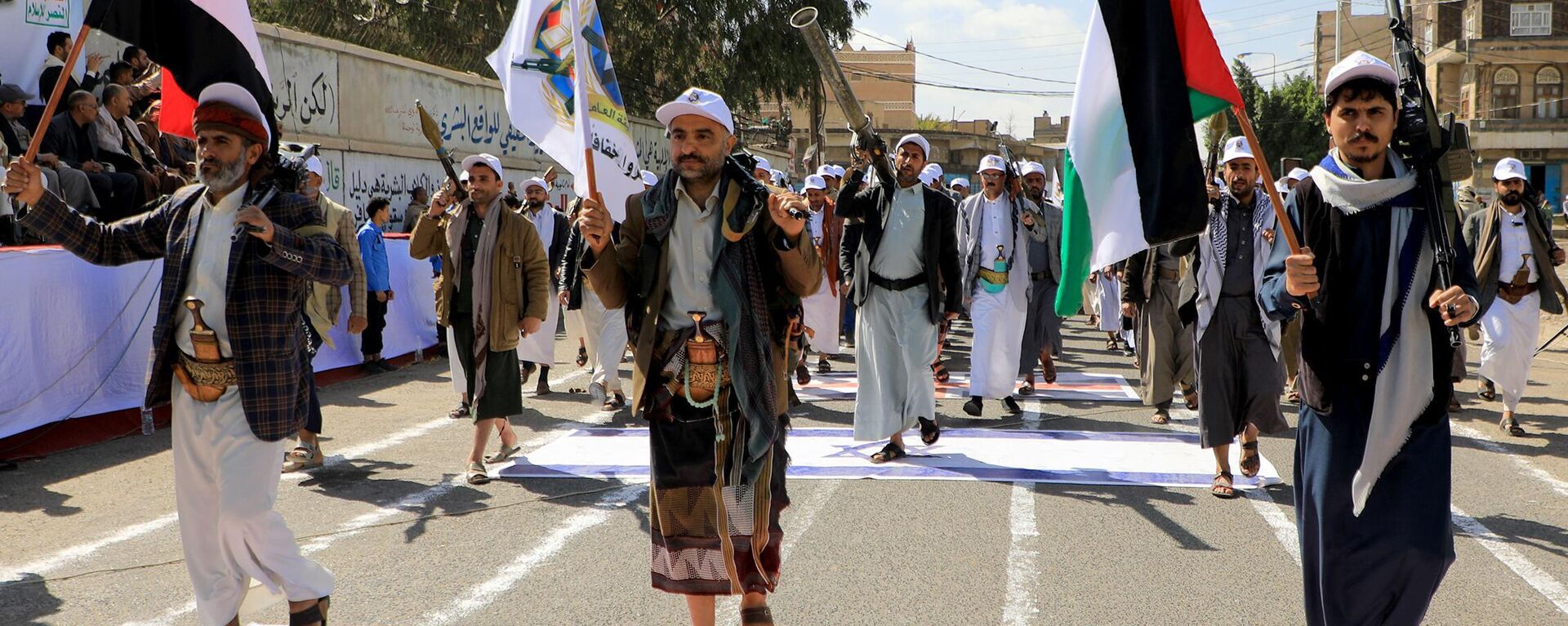 Iemenitas armados passam por cima de uma bandeira dos EUA e de Israel pintada no asfalto na capital controlada pelos houthi, Sanaa, durante uma marcha em apoio aos palestinos em meio a batalha em curso entre militantes de Israel e do Hamas na Faixa de Gaza, 29 de fevereiro de 2024 - Sputnik Brasil, 1920, 15.05.2024