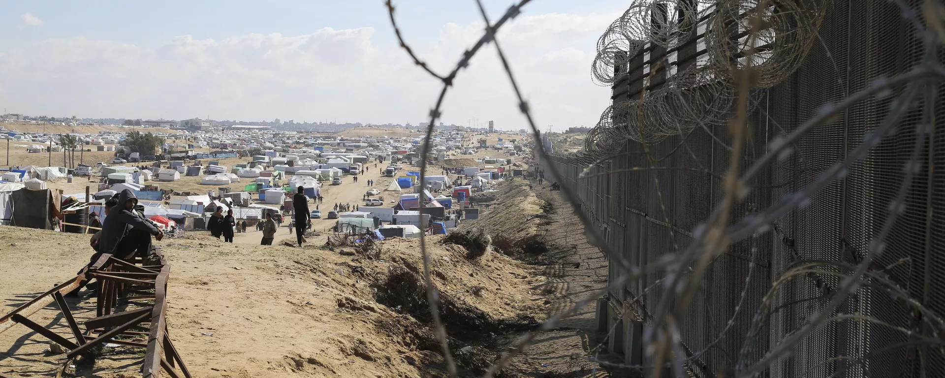 Palestinos deslocados pela ofensiva aérea e terrestre israelense na Faixa de Gaza se sentam próximo à cerca da fronteira com o Egito em Rafah, em 24 de junho de 2024 - Sputnik Brasil, 1920, 13.07.2024