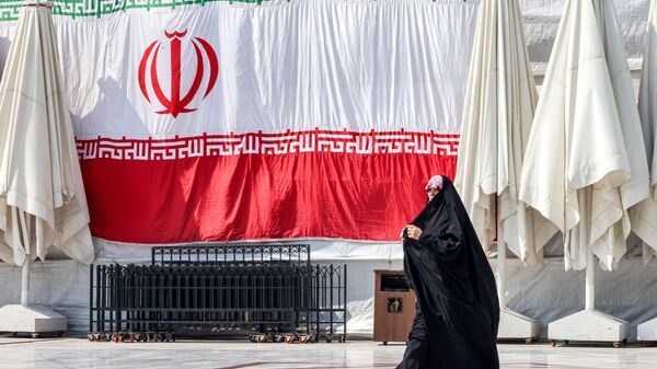 Uma mulher passa por uma bandeira nacional iraniana gigante pendurada do lado de fora da mesquita Emamzadeh Saleh, na praça Tajrish, no norte de Teerã, 12 de março de 2024 - Sputnik Brasil