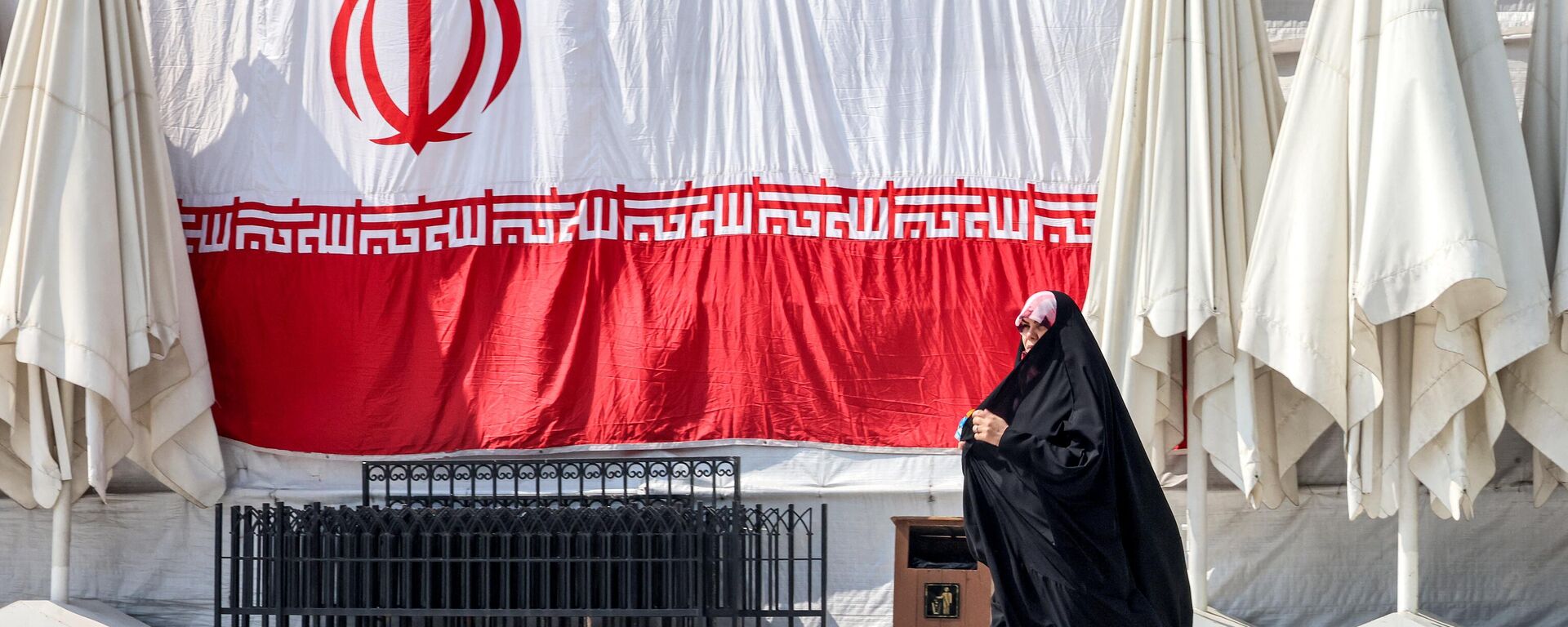 Uma mulher passa por uma bandeira nacional iraniana gigante pendurada do lado de fora da mesquita Emamzadeh Saleh, na praça Tajrish, no norte de Teerã, 12 de março de 2024 - Sputnik Brasil, 1920, 23.05.2024