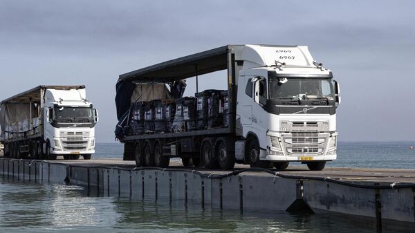 Caminhões carregados com ajuda humanitária dos Emirados Árabes Unidos e da Agência dos Estados Unidos para o Desenvolvimento Internacional cruzam o Píer Trident antes de chegar à praia da Faixa de Gaza, 17 de maio de 2024 - Sputnik Brasil