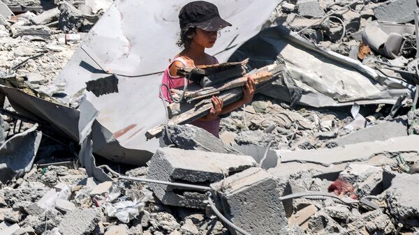 Uma menina caminha com madeira recuperada entre os escombros no local de um prédio que foi atingido por bombardeios israelenses no bairro de Sabra, no sul da Cidade de Gaza, em 27 de junho de 2024 - Sputnik Brasil