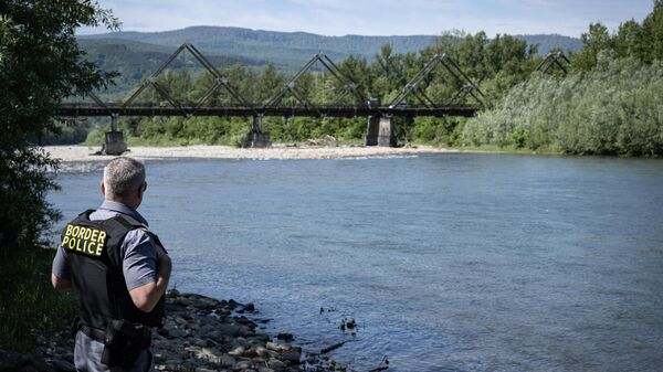 Um policial de fronteira romeno inspeciona a margem do rio Tisa, tendo como pano de fundo a ponte de madeira que liga a Romênia e a Ucrânia, perto do posto fronteiriço de Sighetu Marmatiei, 17 de maio de 2024 - Sputnik Brasil