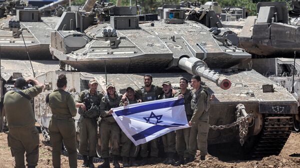 Soldados do exército israelense posam para uma foto com uma bandeira nacional israelense em frente a um tanque de batalha principal posicionado no sul de Israel, perto da fronteira com a Faixa de Gaza, 9 de maio de 2024 - Sputnik Brasil