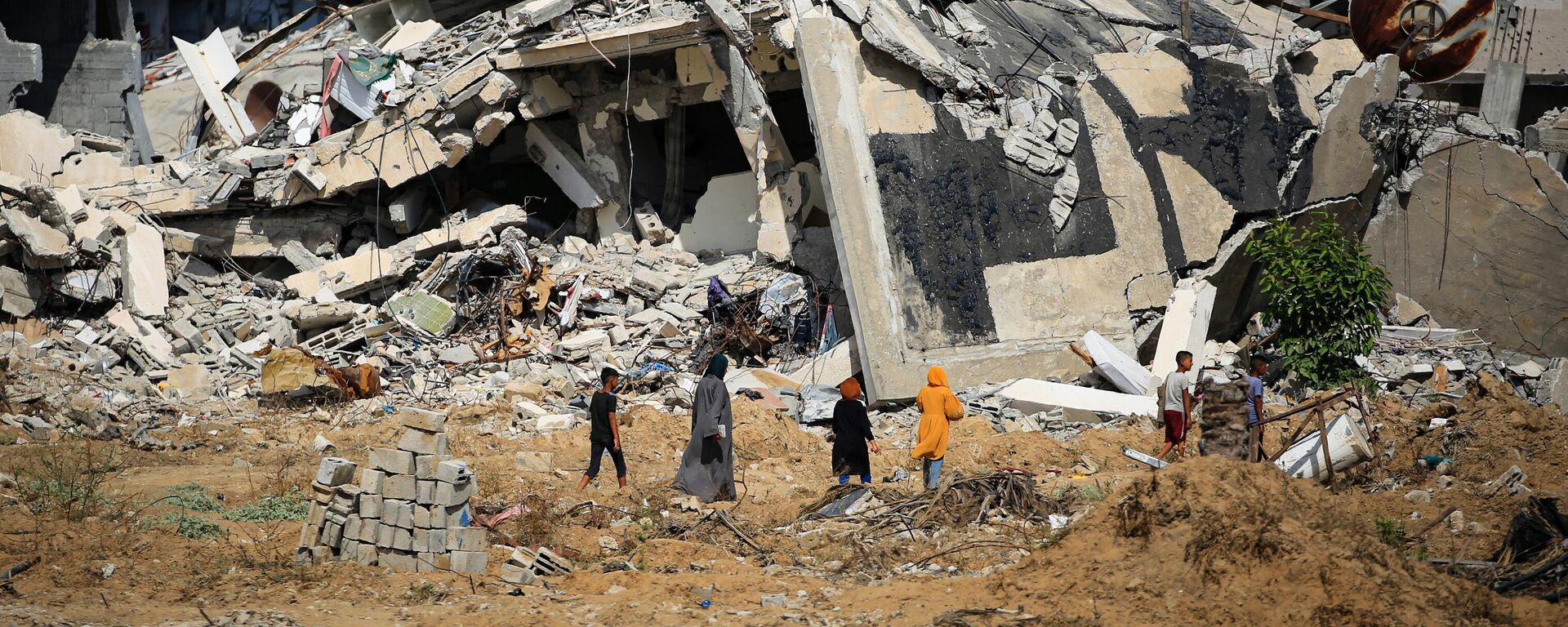 Mulheres e meninos palestinos caminham em direção a prédios destruídos, enquanto alguns moradores retornam à cidade de Khan Yunis, no sul da Faixa de Gaza, 30 de junho de 2024 - Sputnik Brasil, 1920, 01.03.2025