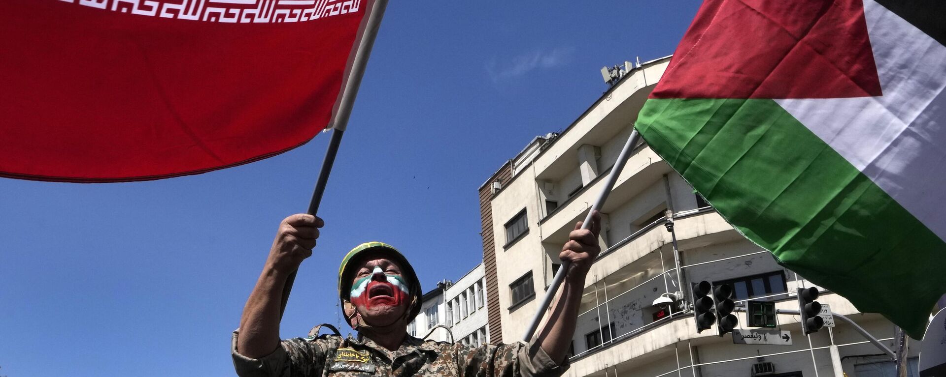 Com o rosto pintado nas cores da bandeira iraniana, um homem chora enquanto agita bandeiras iranianas e palestinas no comício anual para marcar o Dia de Quds, ou Dia de Jerusalém, em apoio aos palestinos, em Teerã, Irã, 5 de abril de 2024 - Sputnik Brasil, 1920, 13.10.2025