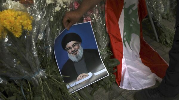 Um homem coloca um pôster do líder do Hezbollah, Sayyed Hassan Nasrallah, perto de buquês de flores em frente à Embaixada do Líbano em Teerã - Sputnik Brasil