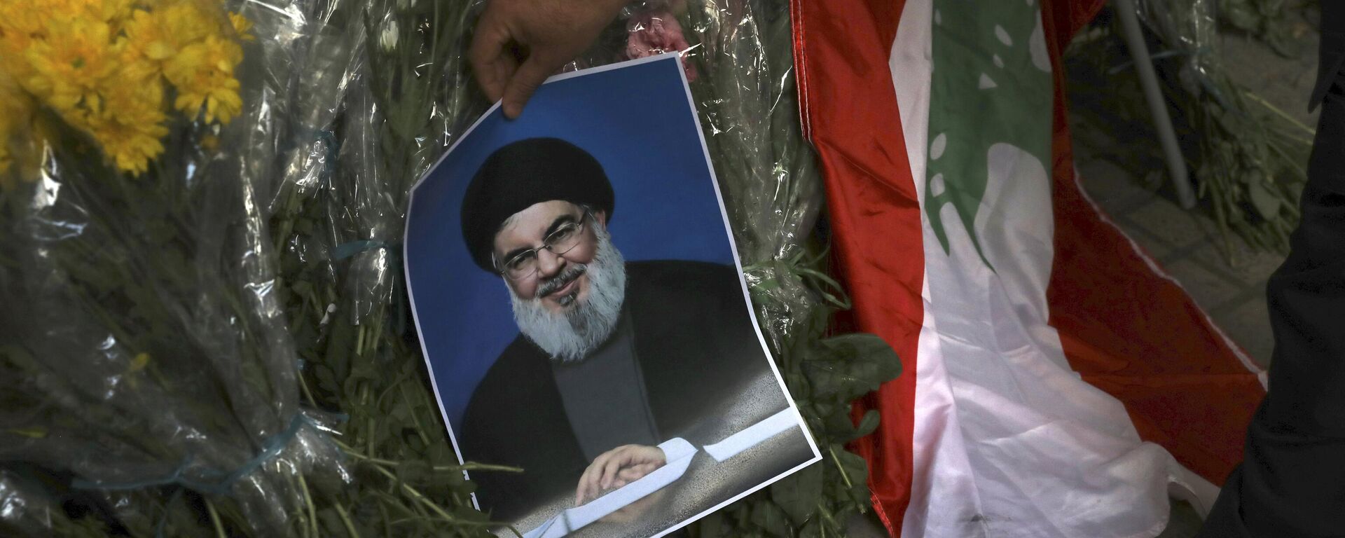 Um homem coloca um pôster do líder do Hezbollah, Sayyed Hassan Nasrallah, perto de buquês de flores em frente à Embaixada do Líbano em Teerã - Sputnik Brasil, 1920, 28.09.2024