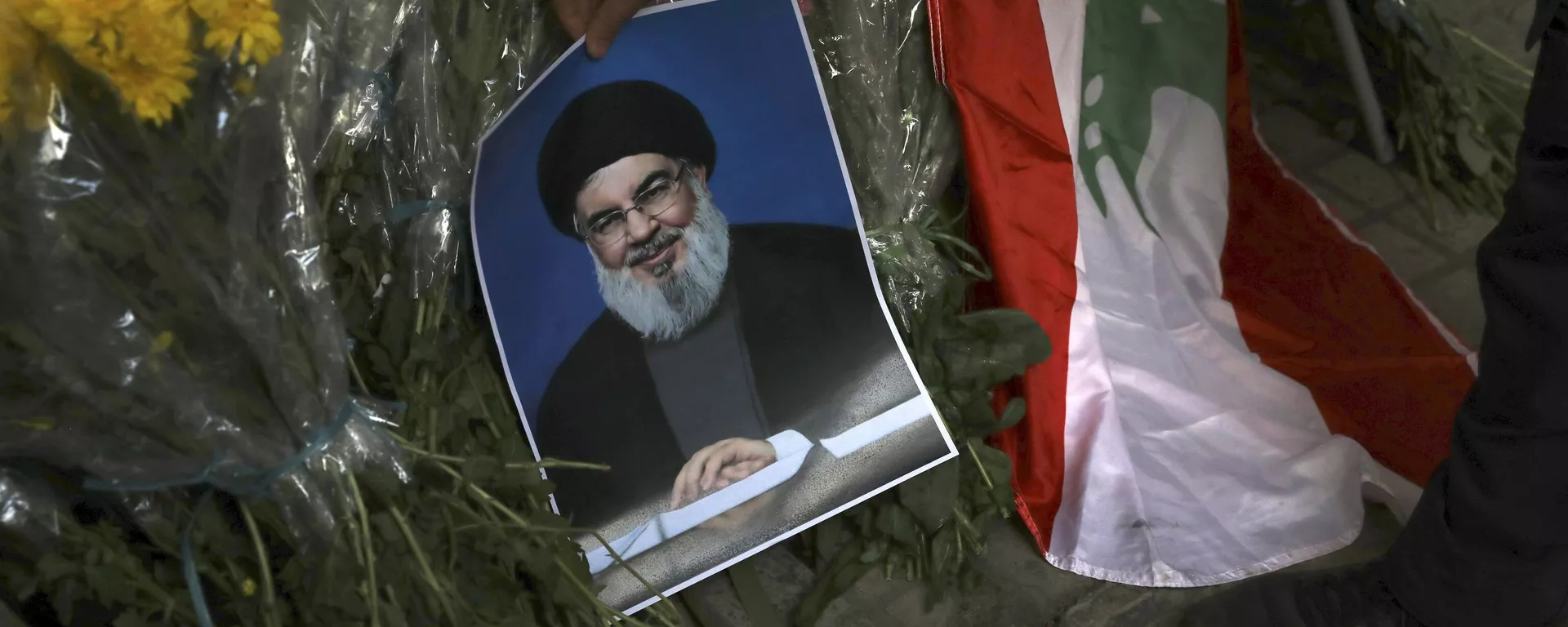 Um homem coloca um pôster do líder do Hezbollah, Sayyed Hassan Nasrallah, perto de buquês de flores em frente à Embaixada do Líbano em Teerã - Sputnik Brasil, 1920, 28.09.2024