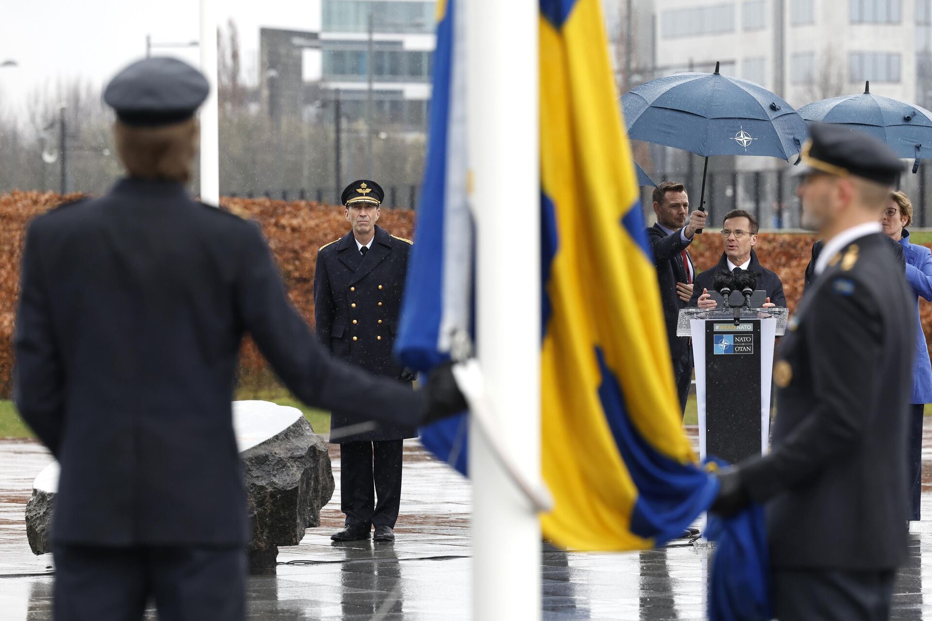 O primeiro-ministro da Suécia, Ulf Kristersson, de centro-direita, fala enquanto militares se preparam para hastear a bandeira da Suécia durante uma cerimônia para marcar a adesão da Suécia à OTAN na sede da OTAN em Bruxelas O primeiro-ministro da Suécia, Ulf Kristersson, de centro-direita, fala enquanto militares se preparam para hastear a bandeira da Suécia durante uma cerimônia para marcar a adesão da Suécia à OTAN na sede da OTAN em Bruxelas