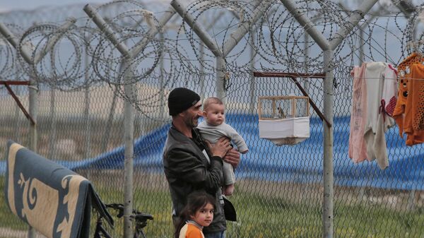 Refugiado sírio em um campo para refugiados em Islahiye, na Turquia, com o filho de 6 meses e a filha de 6 anos, observa o pássaro de estimação da família, suspenso em uma gaiola na cerca de arame farpado do campo, em 16 de março de 2016 - Sputnik Brasil