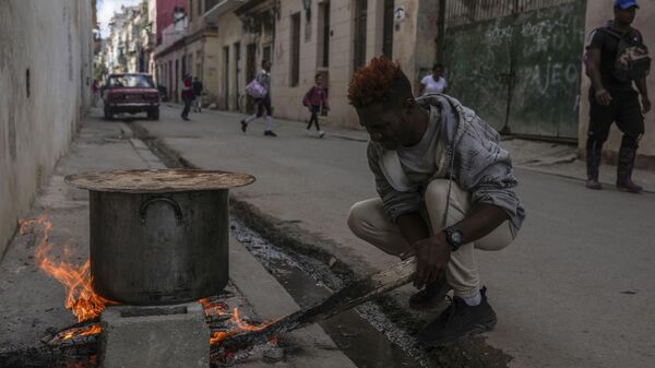 Um homem cozinha sopa sobre uma fogueira na calçada durante um apagão em Havana, Cuba. 4 de dezembro de 2024. - Sputnik Brasil