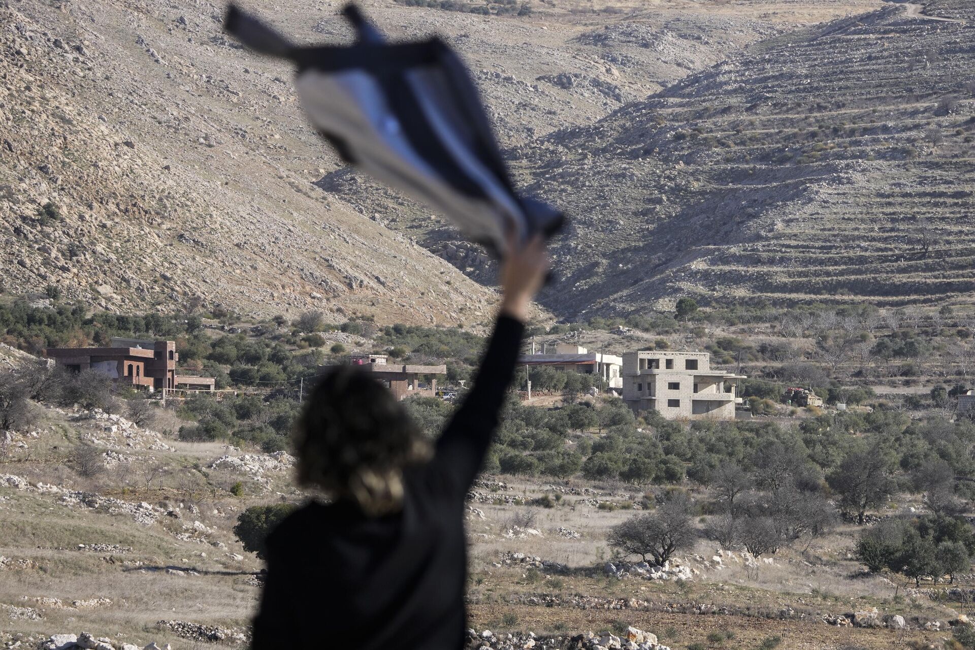 Salma Safadi acena com uma camiseta para sua irmã Sawsan Safadi, que está dentro da zona tampão perto da chamada Linha Alfa que separa as Colinas de Golã controladas por Israel da Síria, na cidade de Majdal Shams, terça-feira, 17 de dezembro de 2024.  - Sputnik Brasil, 1920, 19.12.2024