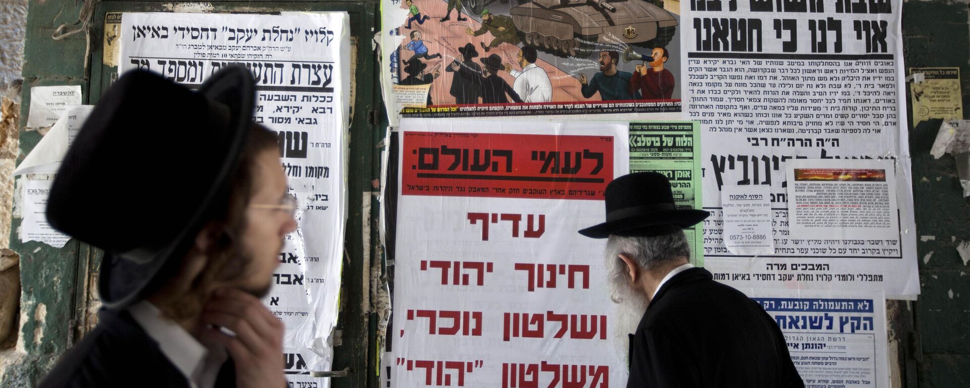 Judeus ultraortodoxos, ou haredi, passam em frente a um mural com publicações que condenam o recrutamento militar, no bairro de Mea Shearim, em Jerusalém, em 14 de julho de 2013 - Sputnik Brasil, 1920, 16.01.2025