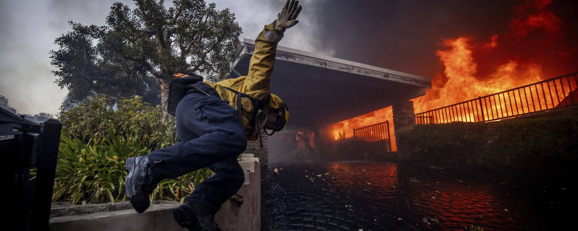 Um bombeiro pula uma cerca enquanto luta contra um incêndio em Los Angeles, EUA - Sputnik Brasil, 1920, 14.01.2025