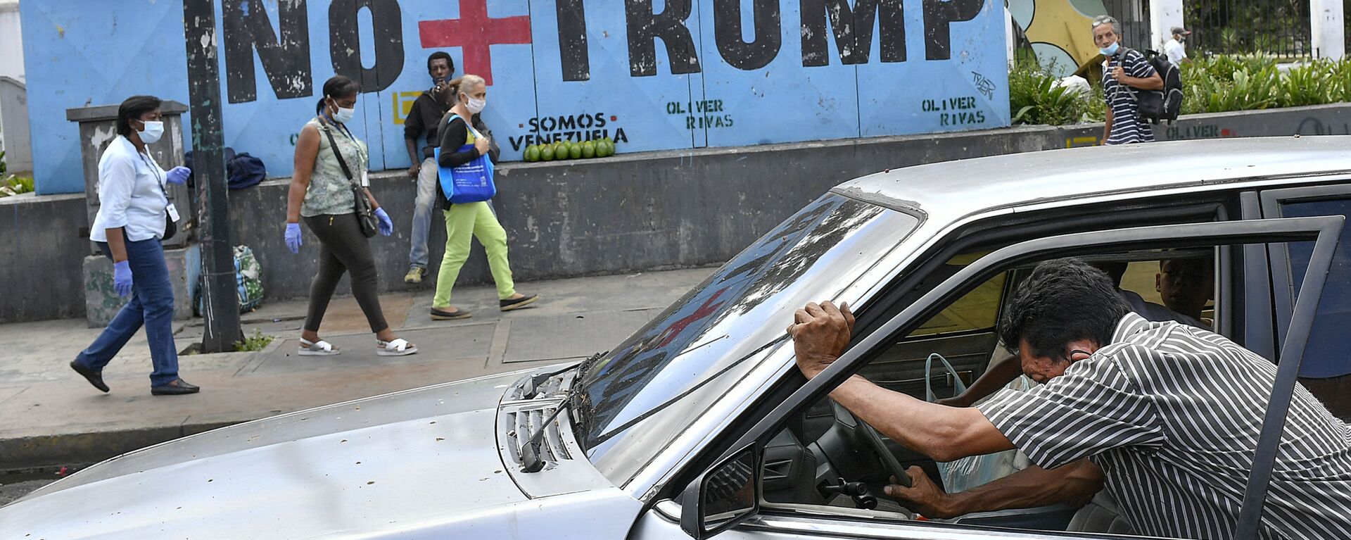 Um homem empurra seu carro que ficou sem gasolina enquanto pessoas usando máscaras de proteção como precaução contra a disseminação da COVID-19 passam por um mural com uma mensagem em espanhol: Chega de Trump em Caracas, Venezuela, 8 de novembro de 2020 - Sputnik Brasil, 1920, 19.01.2025