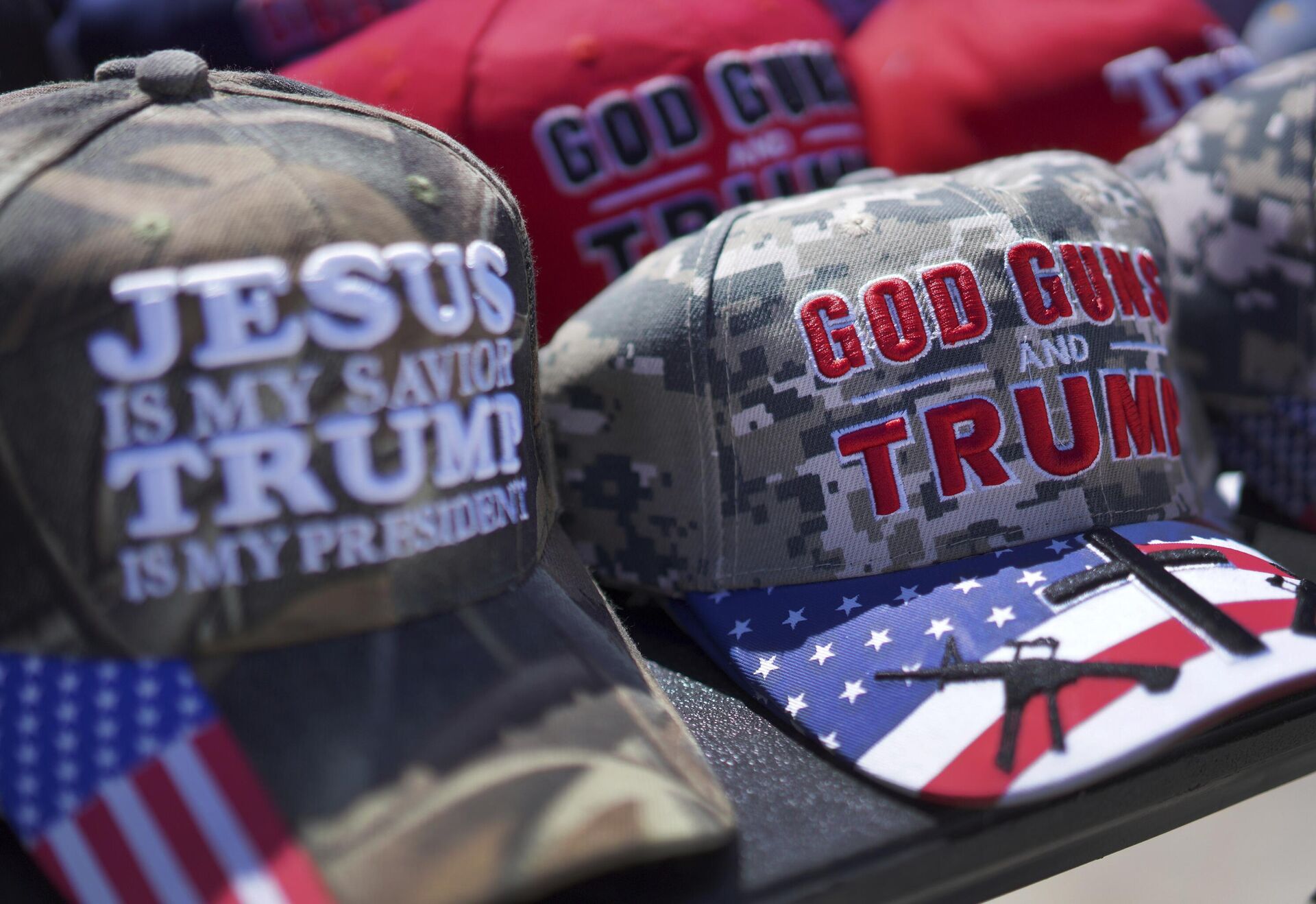 Bonés com as mensagens “Deus, armas e Trump” e “Jesus é meu salvador, Trump é meu presidente” vendidos em um comício da campanha de Donald Trump em Vandalia, Ohio (EUA), 16 de março de 2024. 