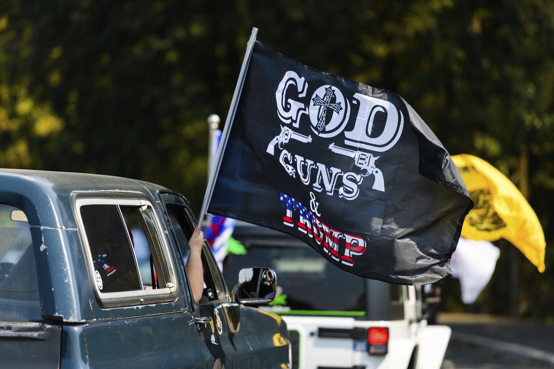 Apoiador de Trump exibe bandeira com a mensagem Deus, armas e Trump, durante carreata de campanha, em Oregon City, EUA (foto de arquivo) 