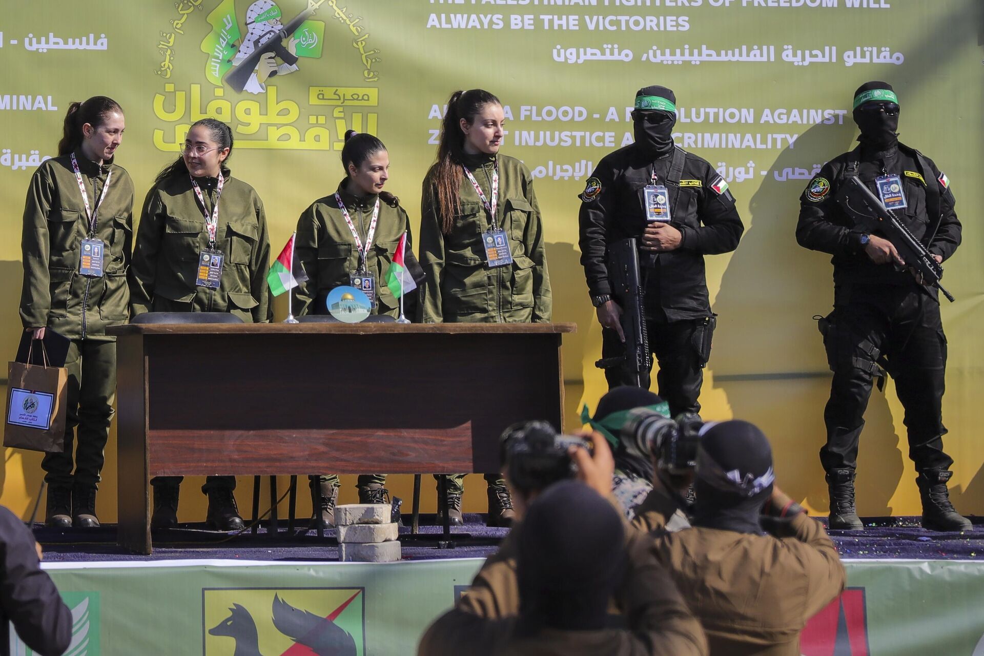 Soldado israelense faz reféns Naama Levy, Daniella Gilboa, Karina Ariev e Liri Albag, sem nenhuma ordem específica, em um palco em frente a uma multidão palestina antes de serem entregues à Cruz Vermelha na Cidade de Gaza, 25 de janeiro de 2025