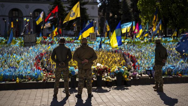 Militares ucranianos ao lado de bandeiras e fotografias ucranianas colocadas em memória de civis e soldados mortos durante o conflito, na Praça da Independência, no centro de Kiev, 20 de abril de 2024 - Sputnik Brasil