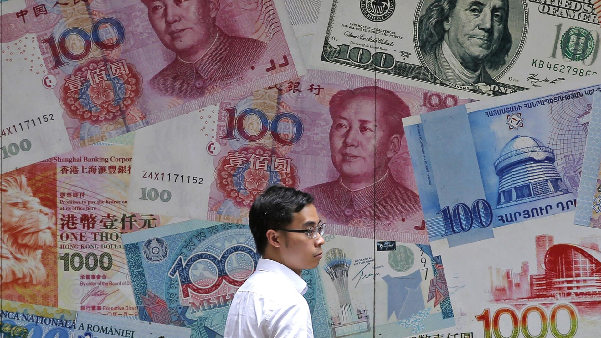 Homem passa por uma casa de câmbio decorada com diferentes notas no Central, um distrito comercial de Hong Kong, em 10 de junho de 2019 - Sputnik Brasil, 1920, 01.07.2025