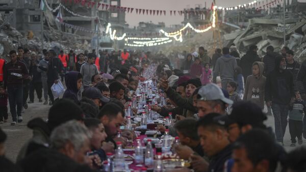 Palestinos sentam-se em uma grande mesa cercada pelos escombros de casas e prédios destruídos enquanto se reúnem para o iftar, a refeição de quebra do jejum, no primeiro dia do Ramadã em Rafah, sul da Faixa de Gaza, sábado, 1º de março de 2025. - Sputnik Brasil