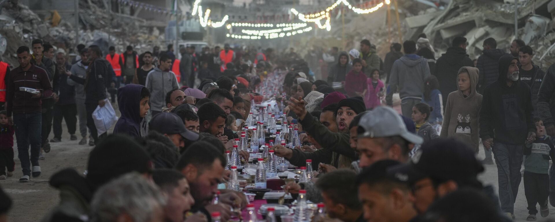 Palestinos sentam-se em uma grande mesa cercada pelos escombros de casas e prédios destruídos enquanto se reúnem para o iftar, a refeição de quebra do jejum, no primeiro dia do Ramadã em Rafah, sul da Faixa de Gaza, sábado, 1º de março de 2025. - Sputnik Brasil, 1920, 04.03.2025