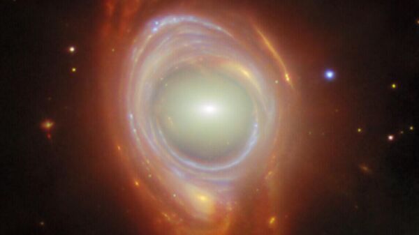 Registro do fenômeno cósmico raro chamado anel de Einstein. O que a princípio parece ser uma única galáxia de formato estranho é, na verdade, duas galáxias separadas por uma grande distância. A galáxia mais próxima do primeiro plano fica no centro da imagem, enquanto a galáxia mais distante do fundo parece estar enrolada em volta da galáxia mais próxima, formando um anel. Os anéis de Einstein ocorrem quando a luz de um objeto muito distante é curvada (ou lenteada) em torno de um objeto intermediário massivo - Sputnik Brasil