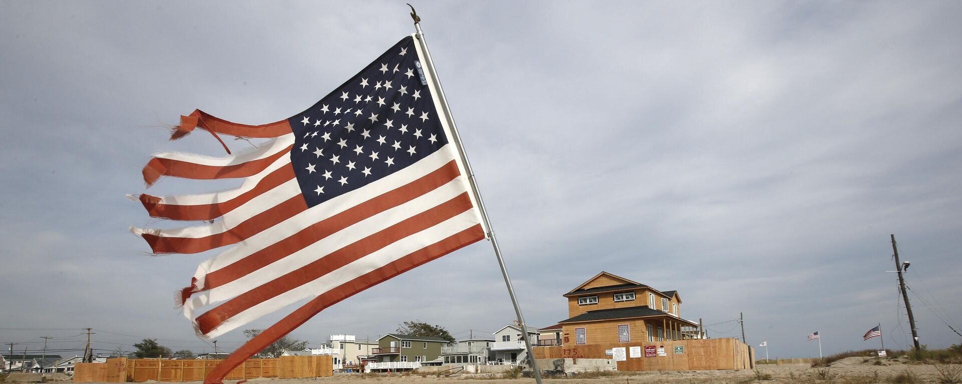 Bandeira dos EUA esfarrapada tremula na areia de um terreno baldio no bairro de Breezy Point, no Queens, em Nova York. EUA, 3 de outubro de 2013 - Sputnik Brasil, 1920, 16.04.2025