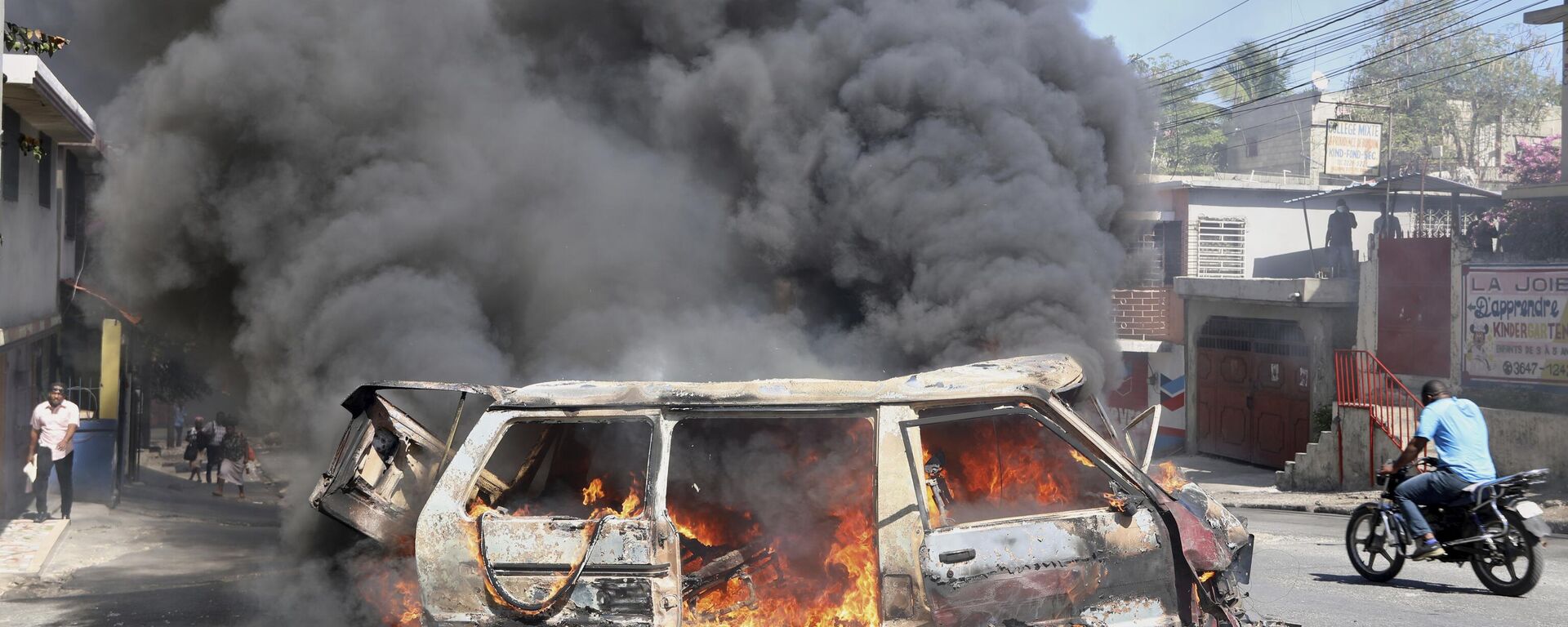 Motociclista passa por um carro em chamas durante um protesto contra a insegurança em Porto Príncipe - Sputnik Brasil, 1920, 16.04.2025