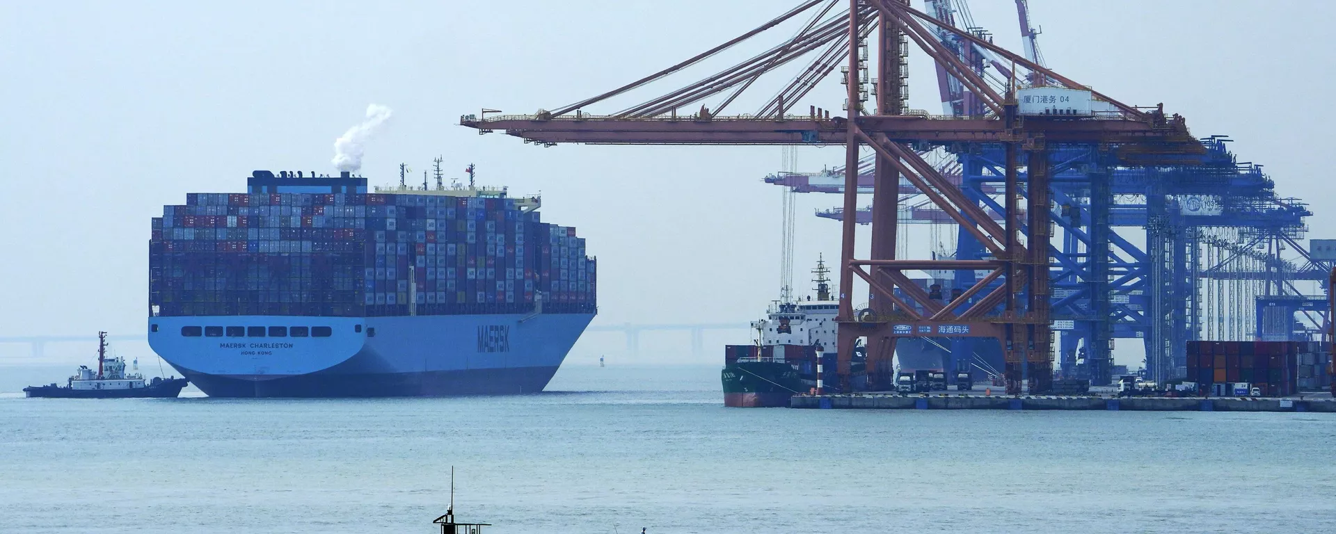 Um homem em um barco pesca enquanto um navio porta-contêineres se prepara para atracar em um porto em Xiamen, na província de Fujian, no sudeste da China, 27 de dezembro de 2023 - Sputnik Brasil, 1920, 27.04.2025