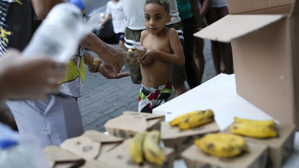 Um menino recebe alimentos doados por um projeto social na favela do Turano, no Rio de Janeiro, 17 de junho de 2024 - Sputnik Brasil