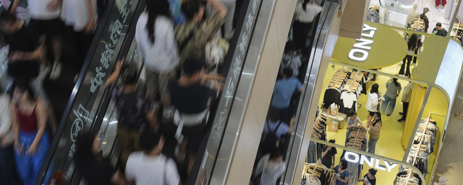 Pessoas sobem escadas rolantes enquanto compradores, à direita no andar de baixo, selecionam roupas em uma loja dentro de um shopping em Pequim, 13 de julho de 2025 - Sputnik Brasil, 1920, 15.07.2025
